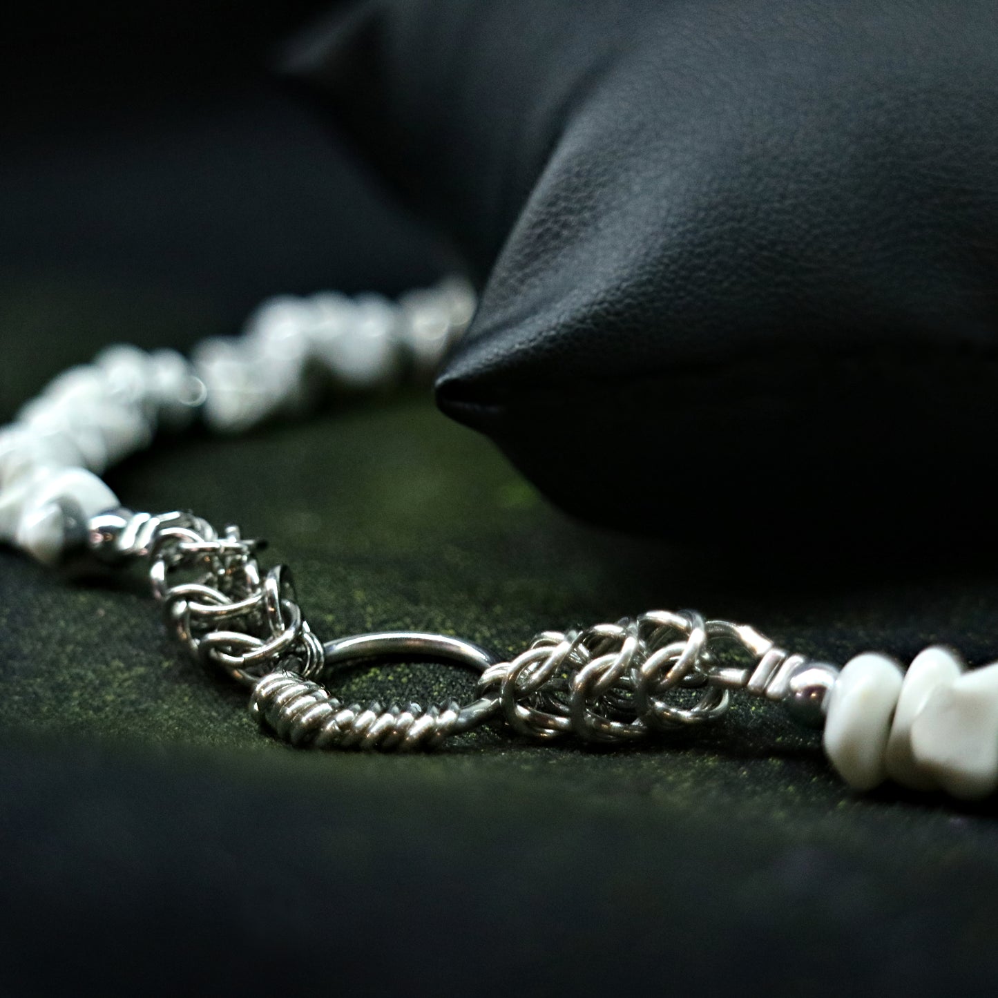 Close-up of the stainless steel chainmail O-ring detail on a white natural-stone necklace against a dark backdrop.