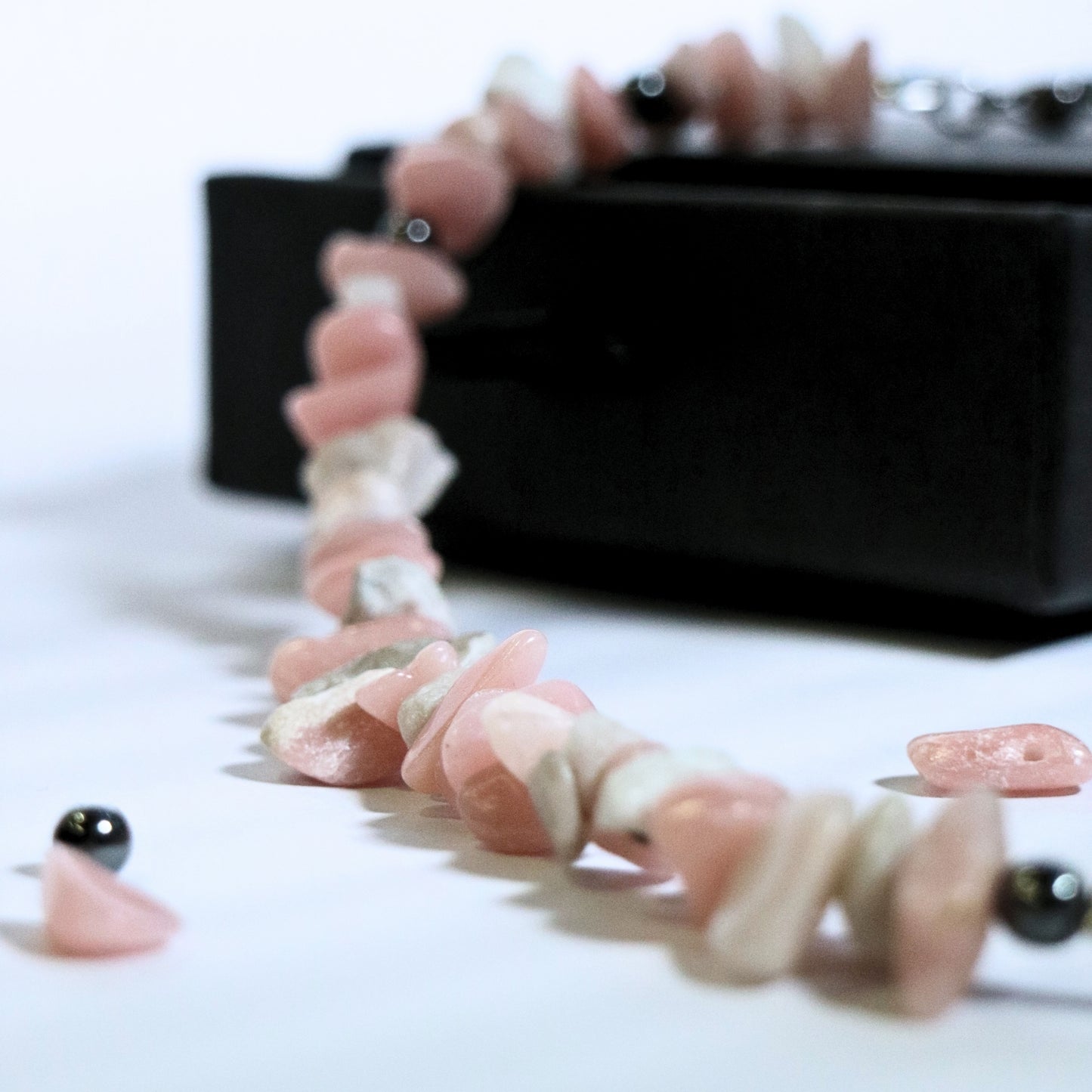 Close-up of the stainless steel chainmail O-ring detail on a dirty pink stone necklace with scattered beads around. 1