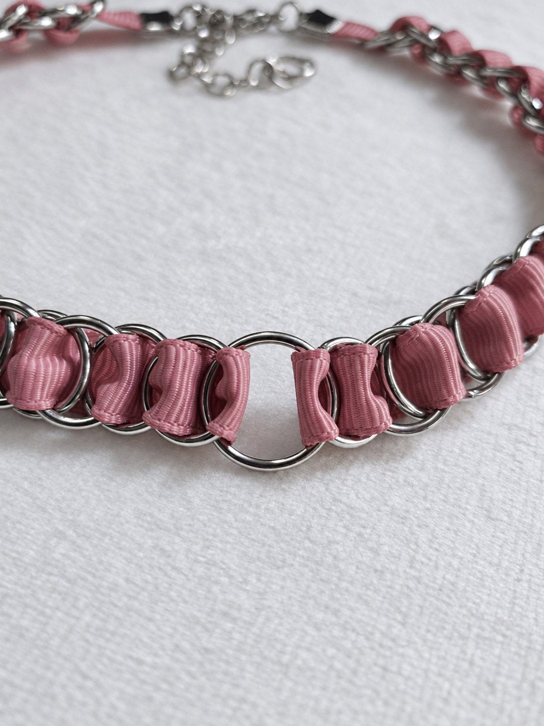DUSTLINK central stainless steel O-ring framed by dusty pink ribbon and interlinked steel rings.