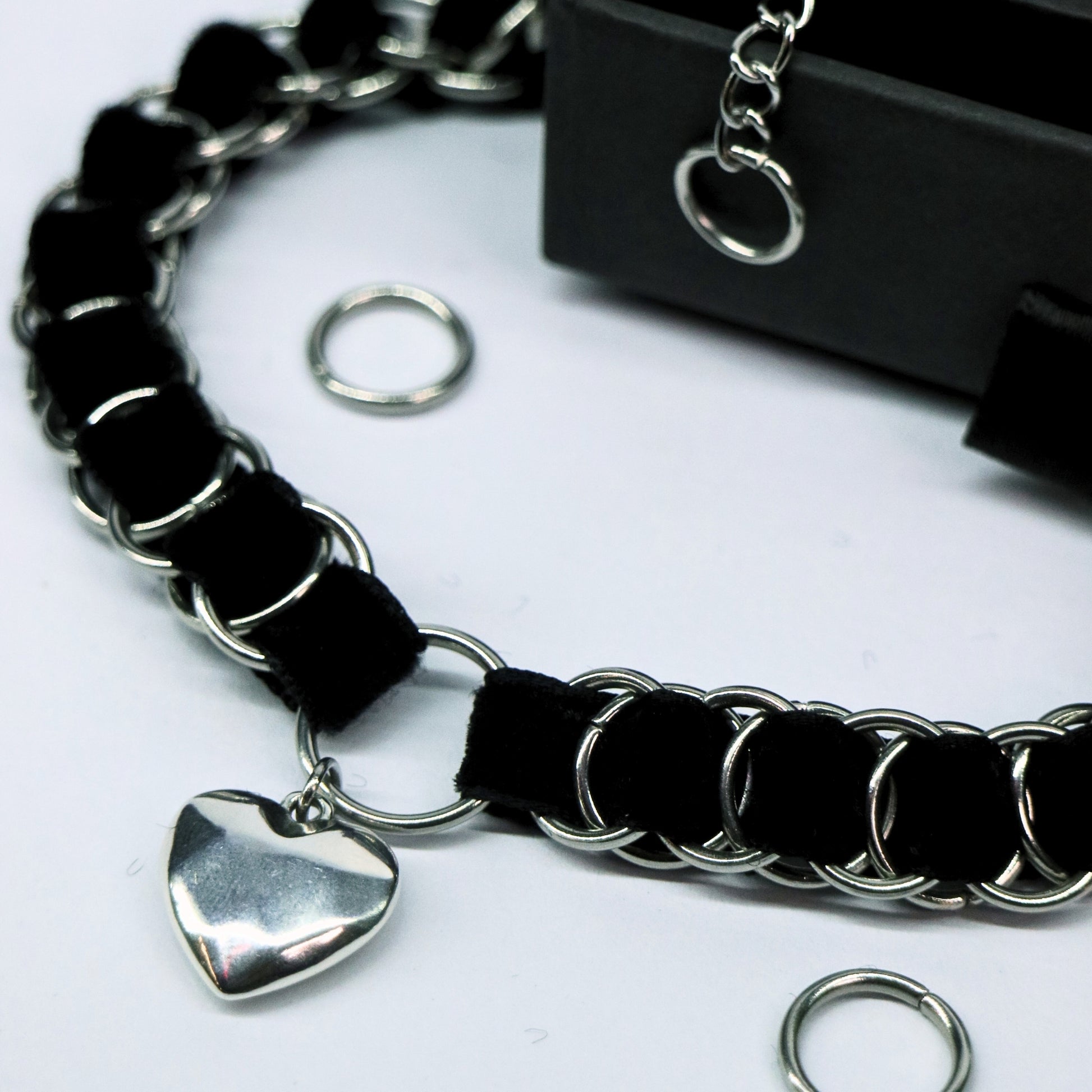 Angled close-up of the black velvet ribbon choker with stainless steel links and heart pendant charm.