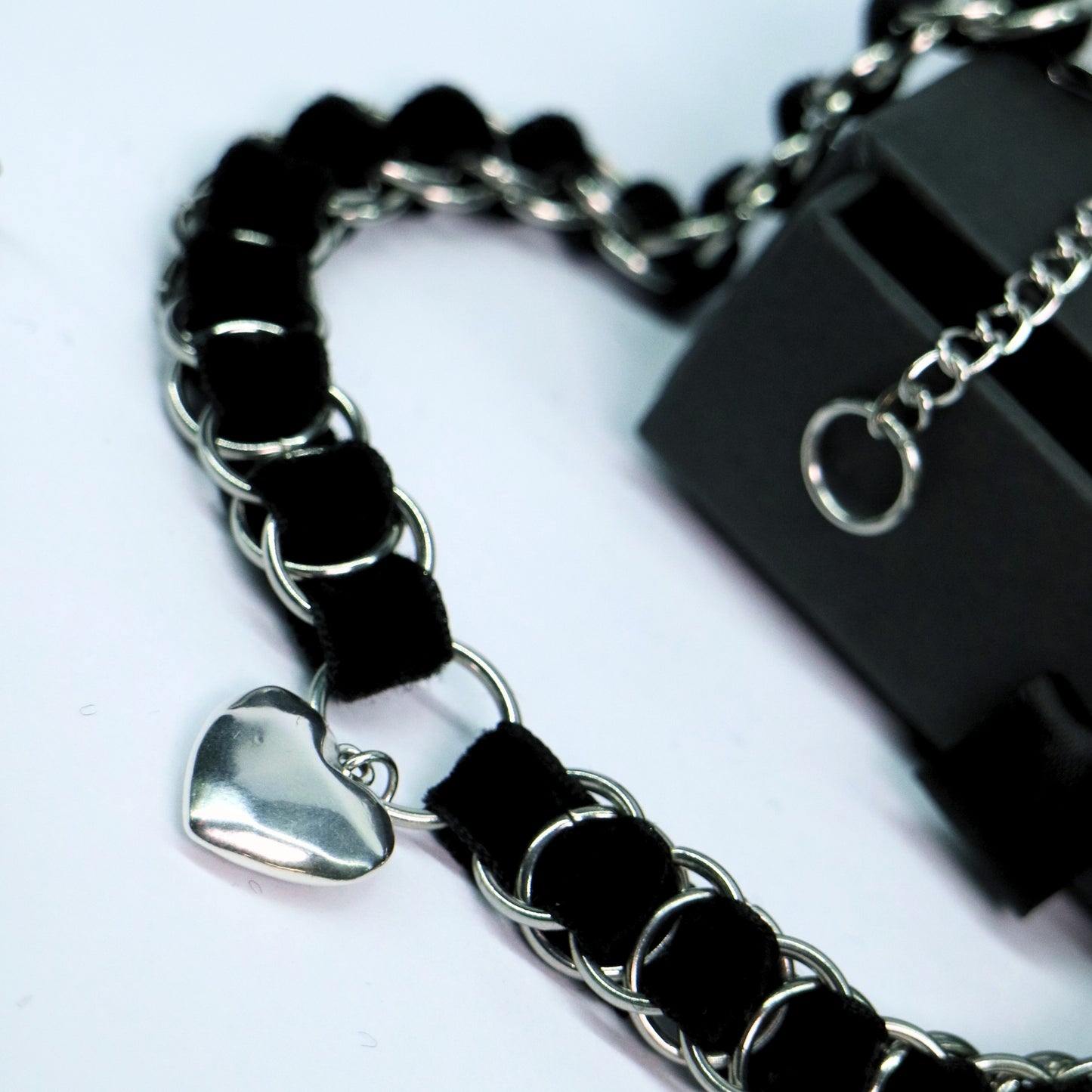 Angled close-up of the black velvet ribbon choker with stainless steel links and heart pendant charm.