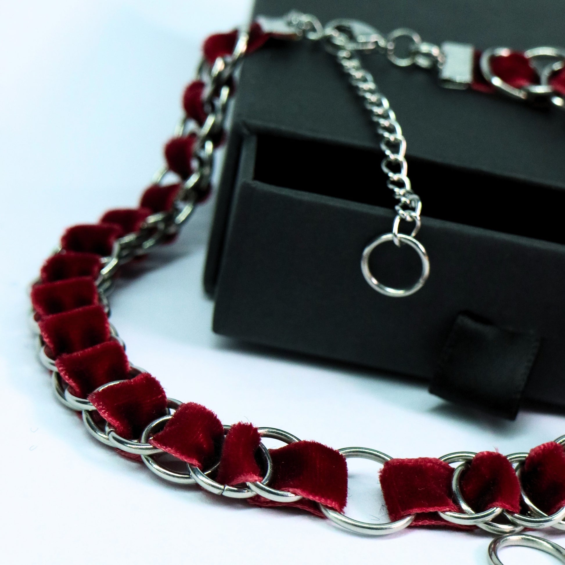 Angled detail view of the blood red velvet ribbon choker with stainless steel ring links and O-ring center.