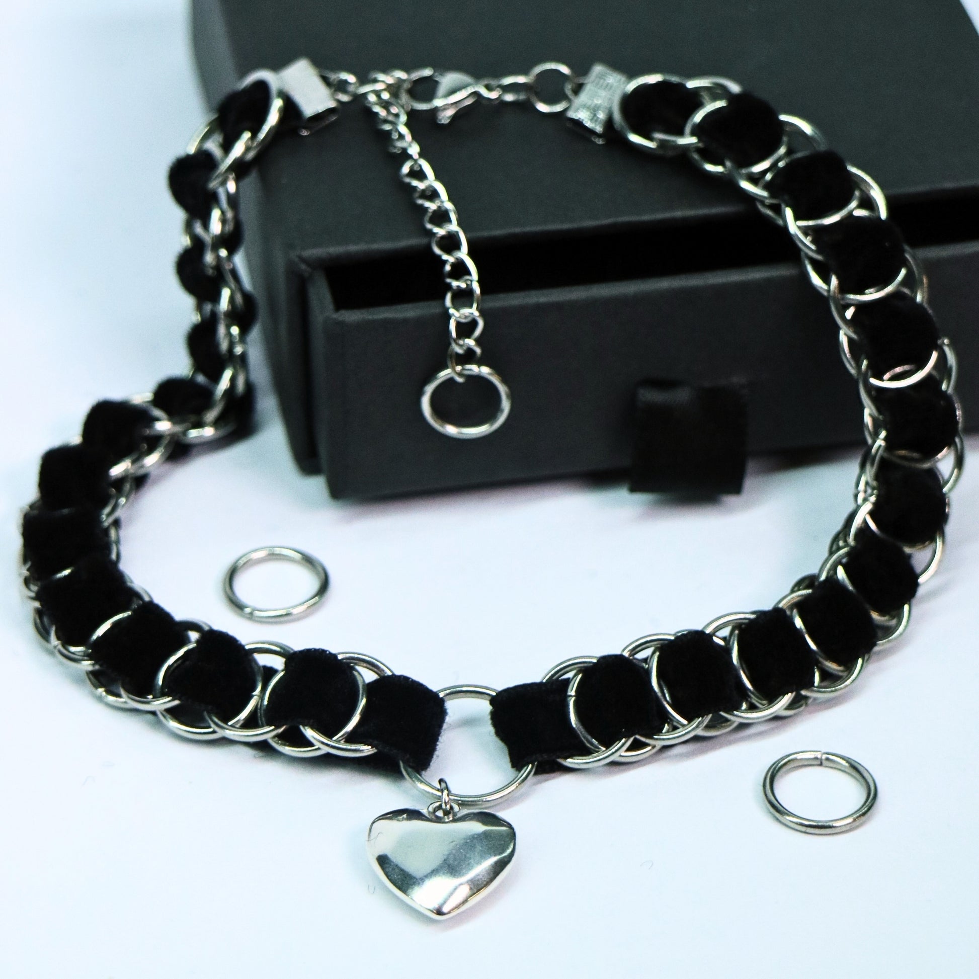 Black velvet ribbon choker woven through stainless steel rings with a heart pendant and O-ring center, shown with gift box and accessories.