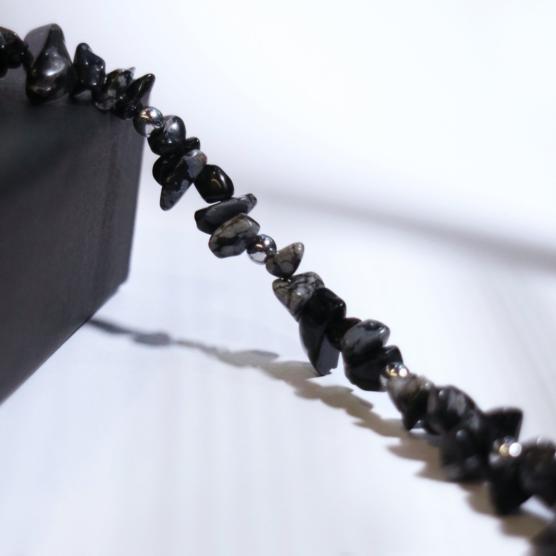 Close-up of a handcrafted black and grey stone necklace with stainless steel beads on a white background next to a black jewelry box