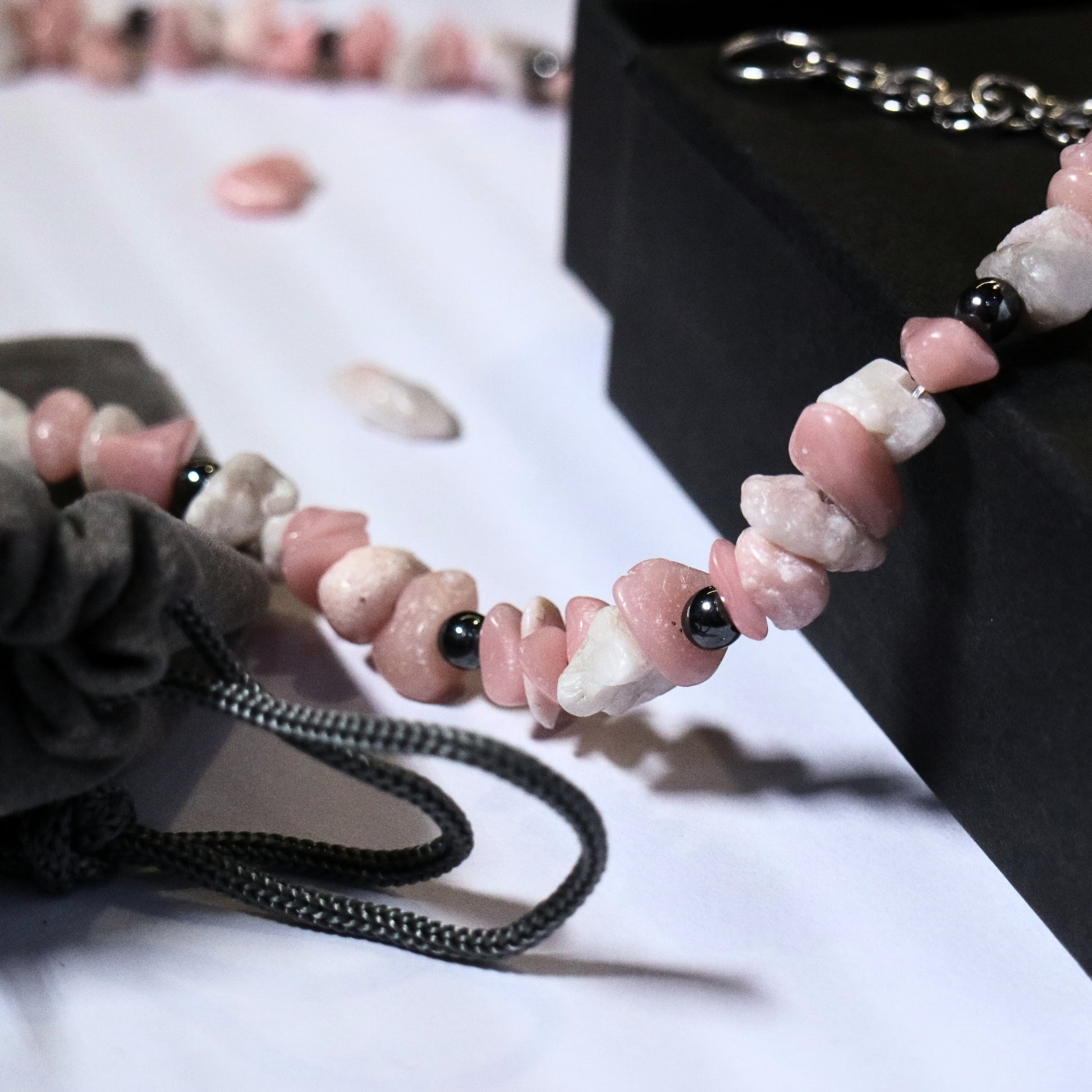 Close-up of a handmade dirty pink and white stone necklace with hematite beads next to a grey drawstring pouch.