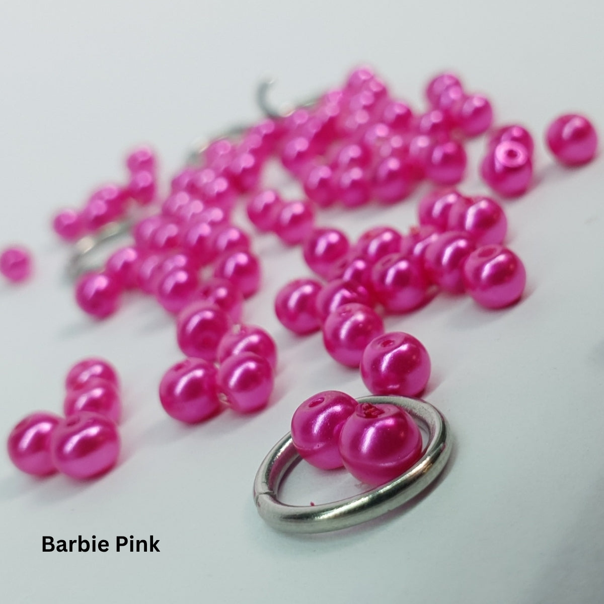 Close-up of bright hot-pink Barbie-tone glass pearls inside stainless steel chainmail links.