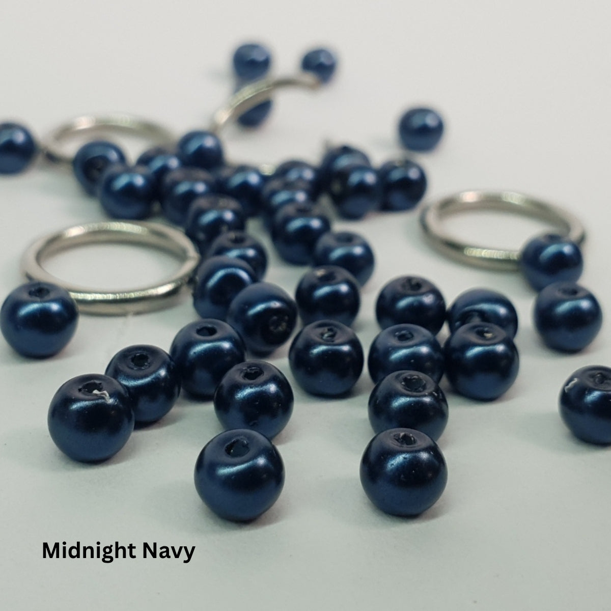 Close-up of dark midnight-navy glass pearls woven through stainless steel chainmail links.