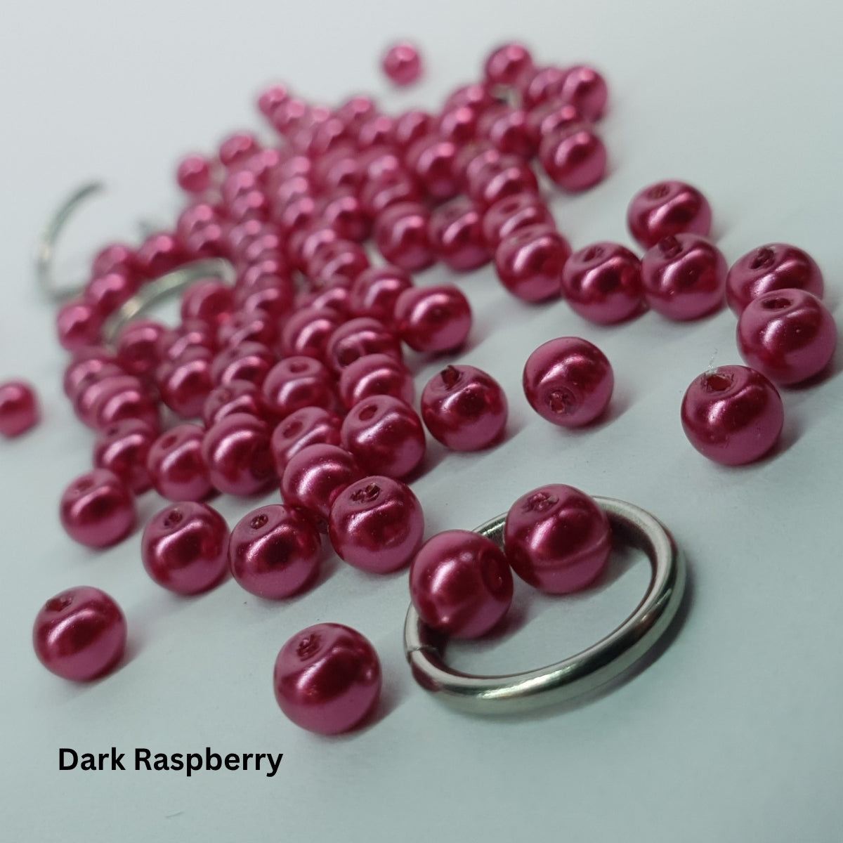 Close-up of deep dark-raspberry glass pearls woven through stainless steel chainmail rings.