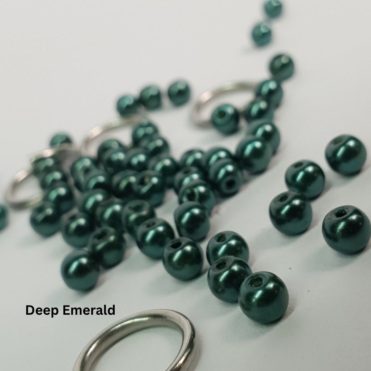 Close-up of deep emerald-green glass pearls paired with stainless steel chainmail rings.