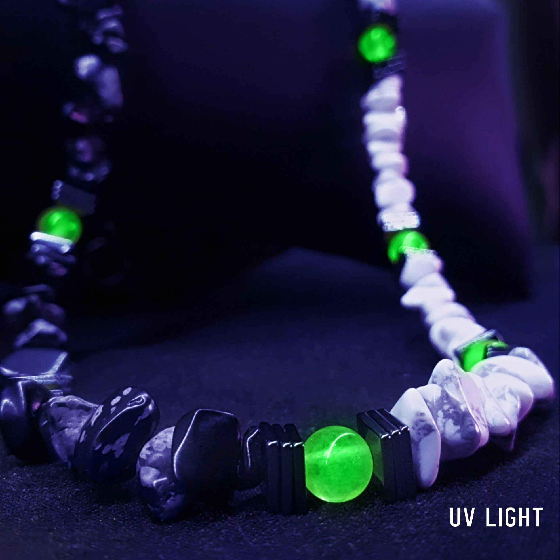 Close-up of the black and white stone necklace under UV light, highlighting the glowing green UV-reactive bead framed by hematite.