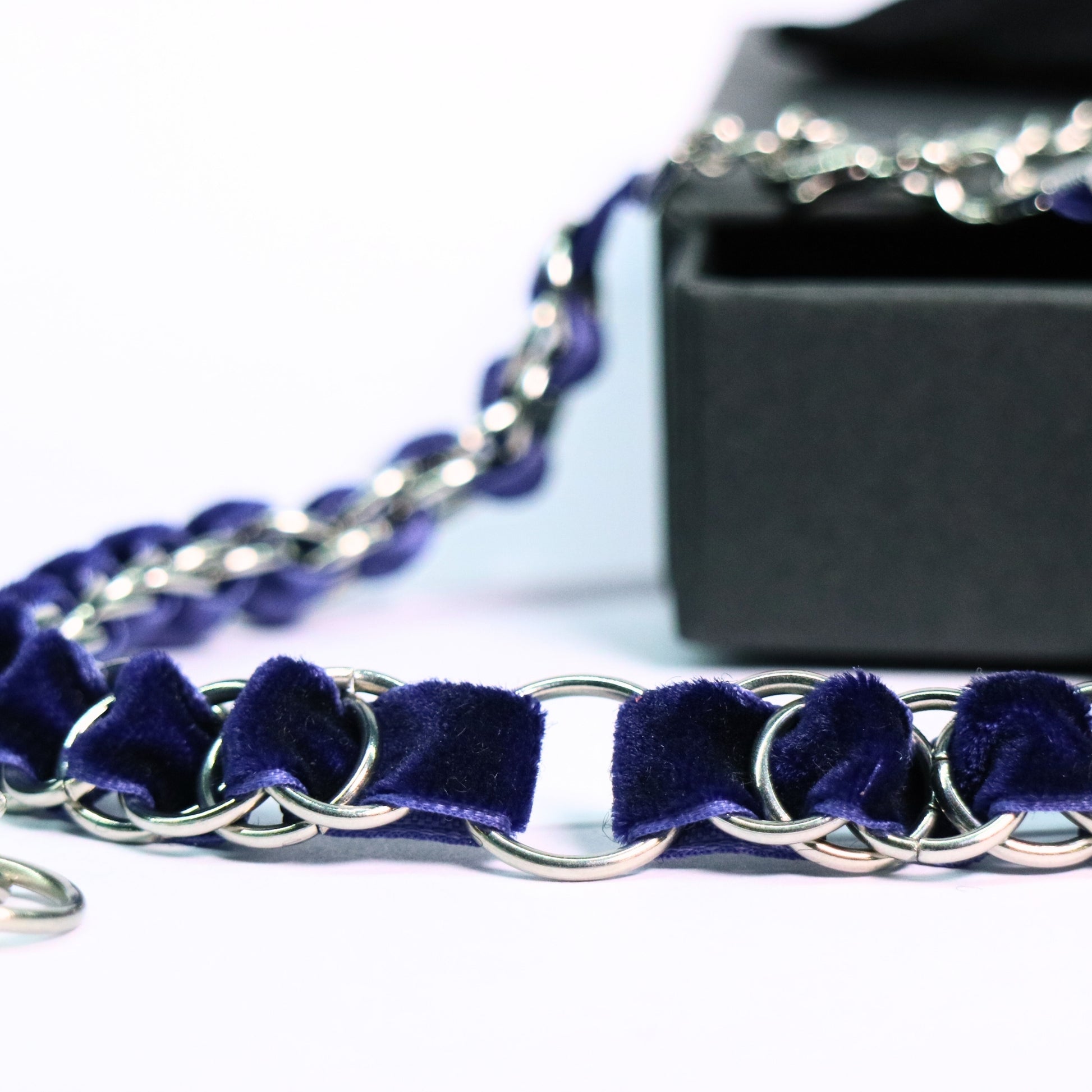 Close-up of the deep blue velvet ribbon choker woven through stainless steel rings, displayed with a black box.