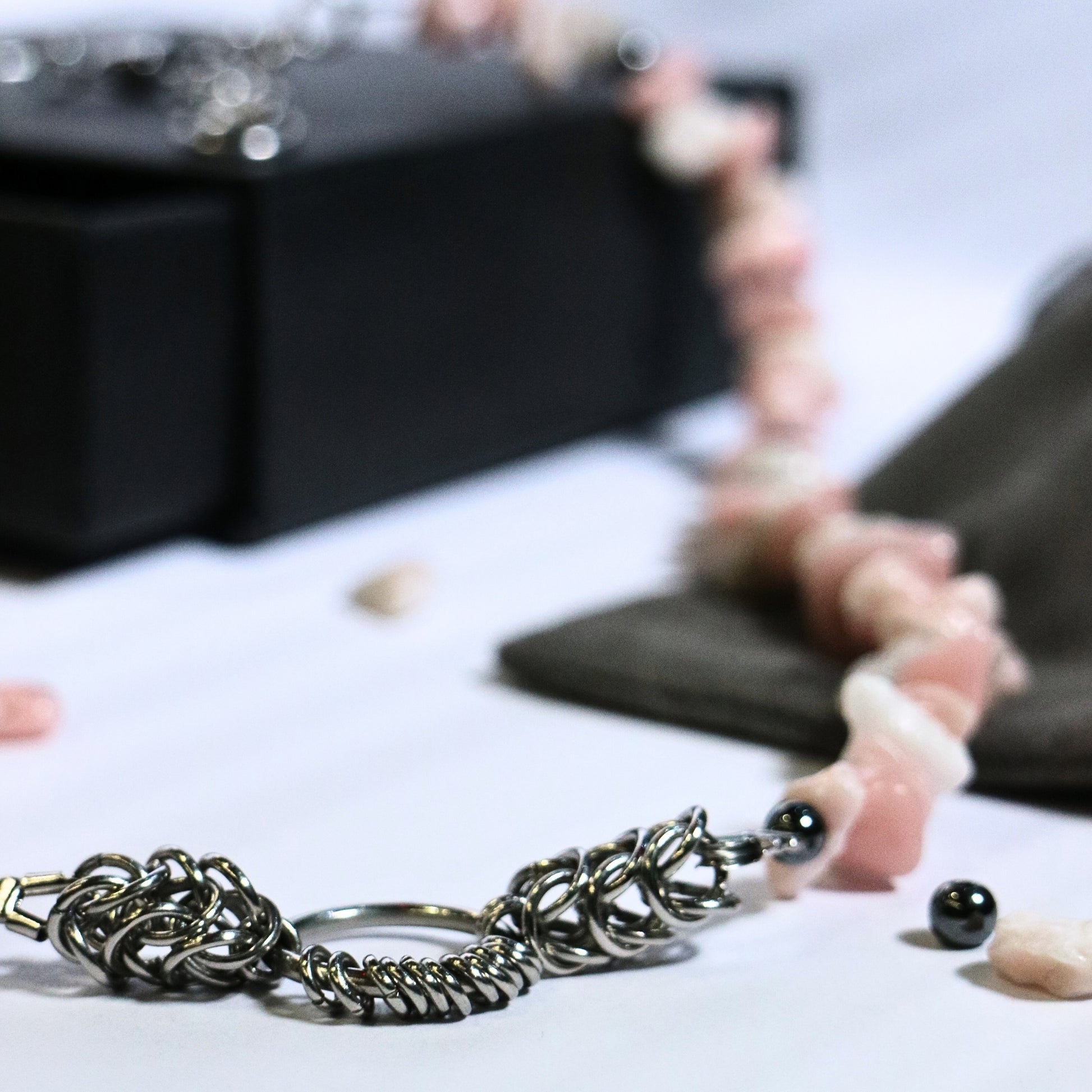 Close-up of the stainless steel chainmail O-ring detail on a dirty pink stone necklace with scattered beads around.