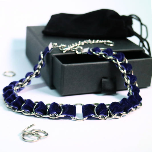 Deep blue velvet ribbon choker woven through stainless steel rings with an O-ring centerpiece, displayed beside a black gift box.