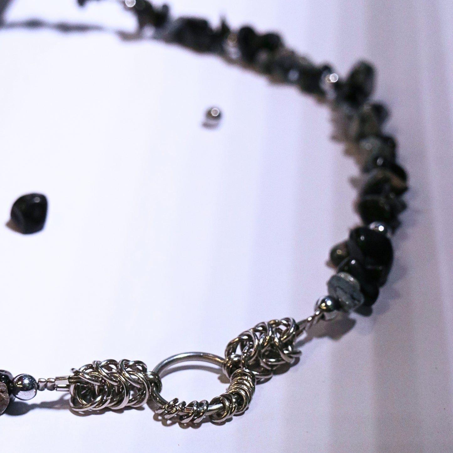 Detail shot of the stainless steel chainmail O-ring centerpiece on a black and grey stone necklace, displayed on a white surface