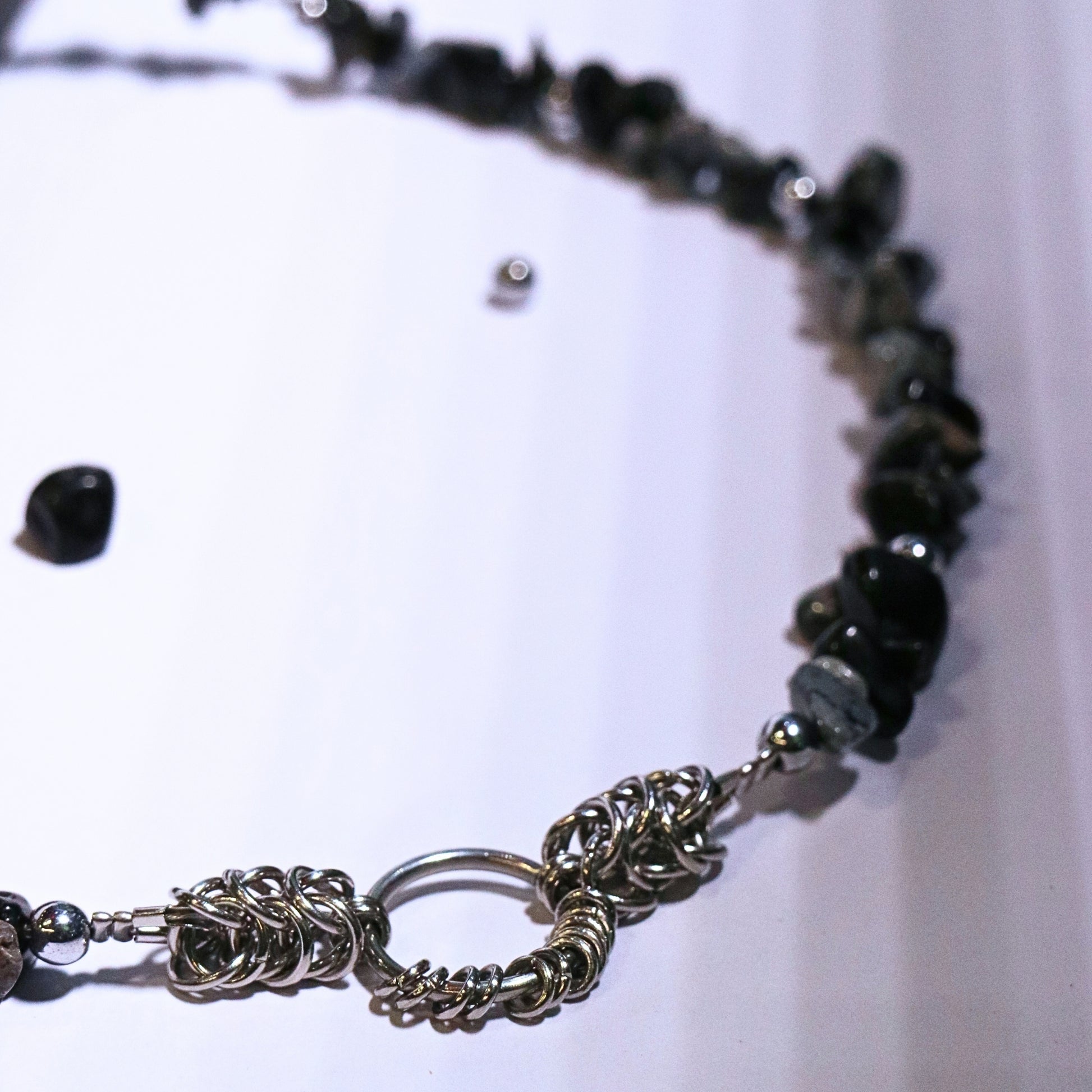 Detail shot of the stainless steel chainmail O-ring centerpiece on a black and grey stone necklace, displayed on a white surface