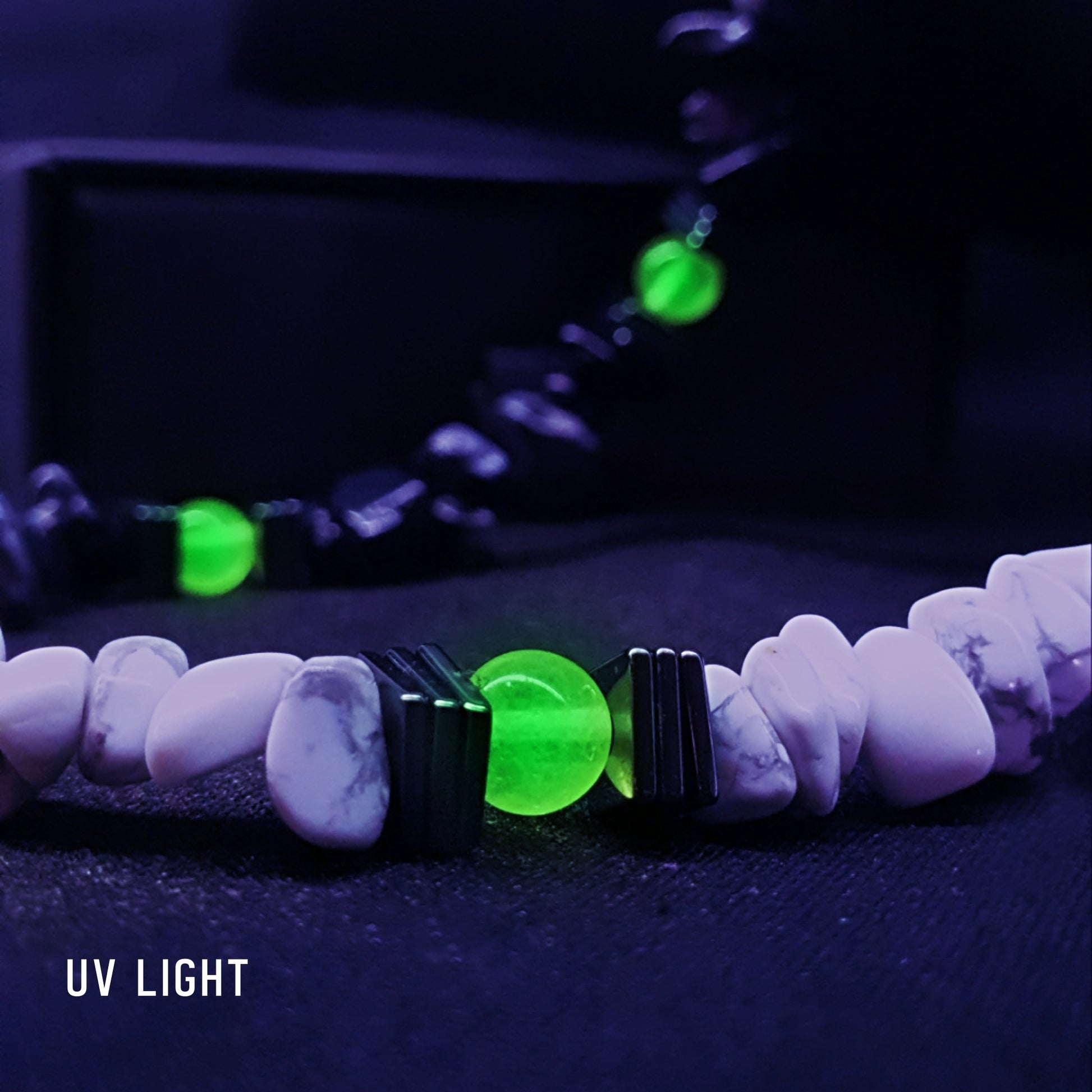 Front view of the yin-yang stone necklace glowing under UV light with vivid green UV-reactive beads and gunmetal hematite accents.