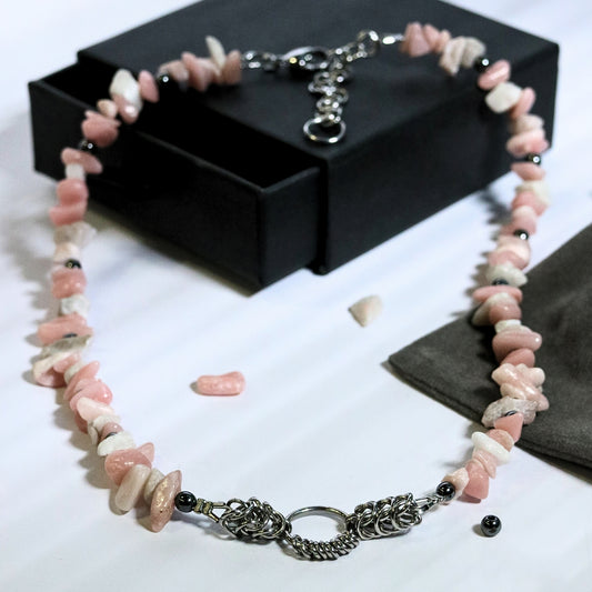 Full display of a dirty pink and white natural-stone necklace with stainless steel chainmail centerpiece styled around a black jewelry box.