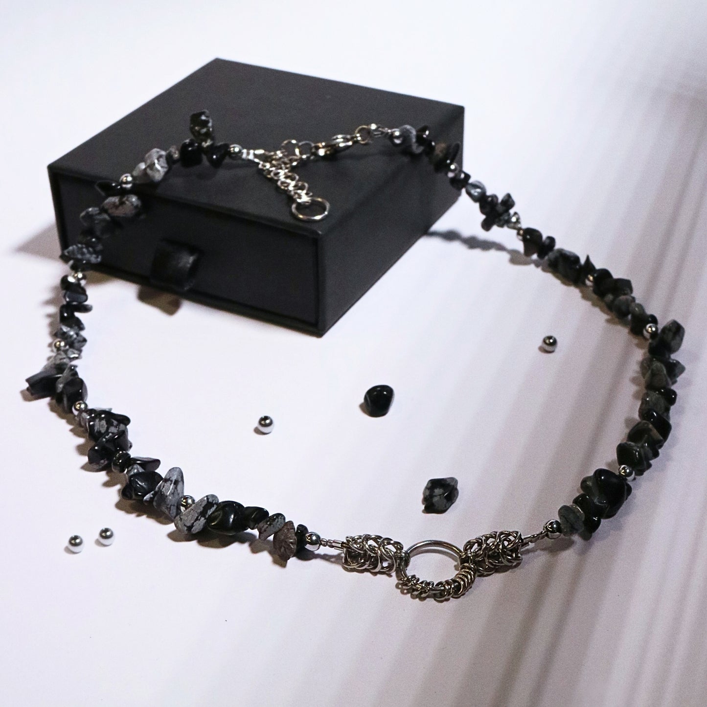 Full product display of a handmade black and grey stone necklace with stainless steel chainmail accents, styled around a black jewelry box