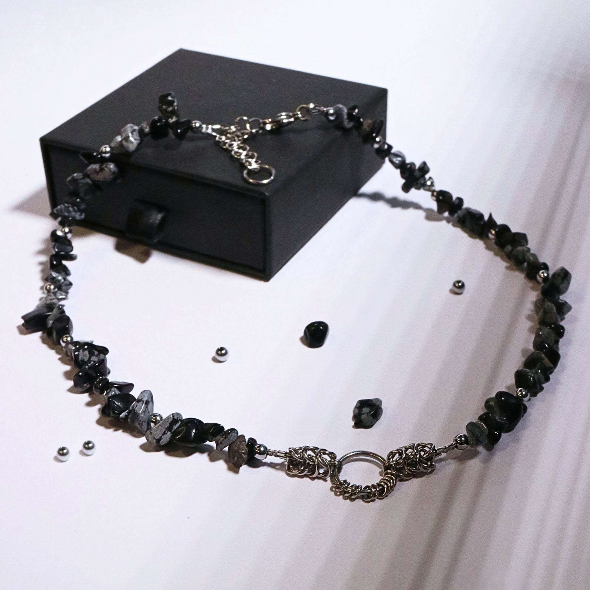 Full product display of a handmade black and grey stone necklace with stainless steel chainmail accents, styled around a black jewelry box