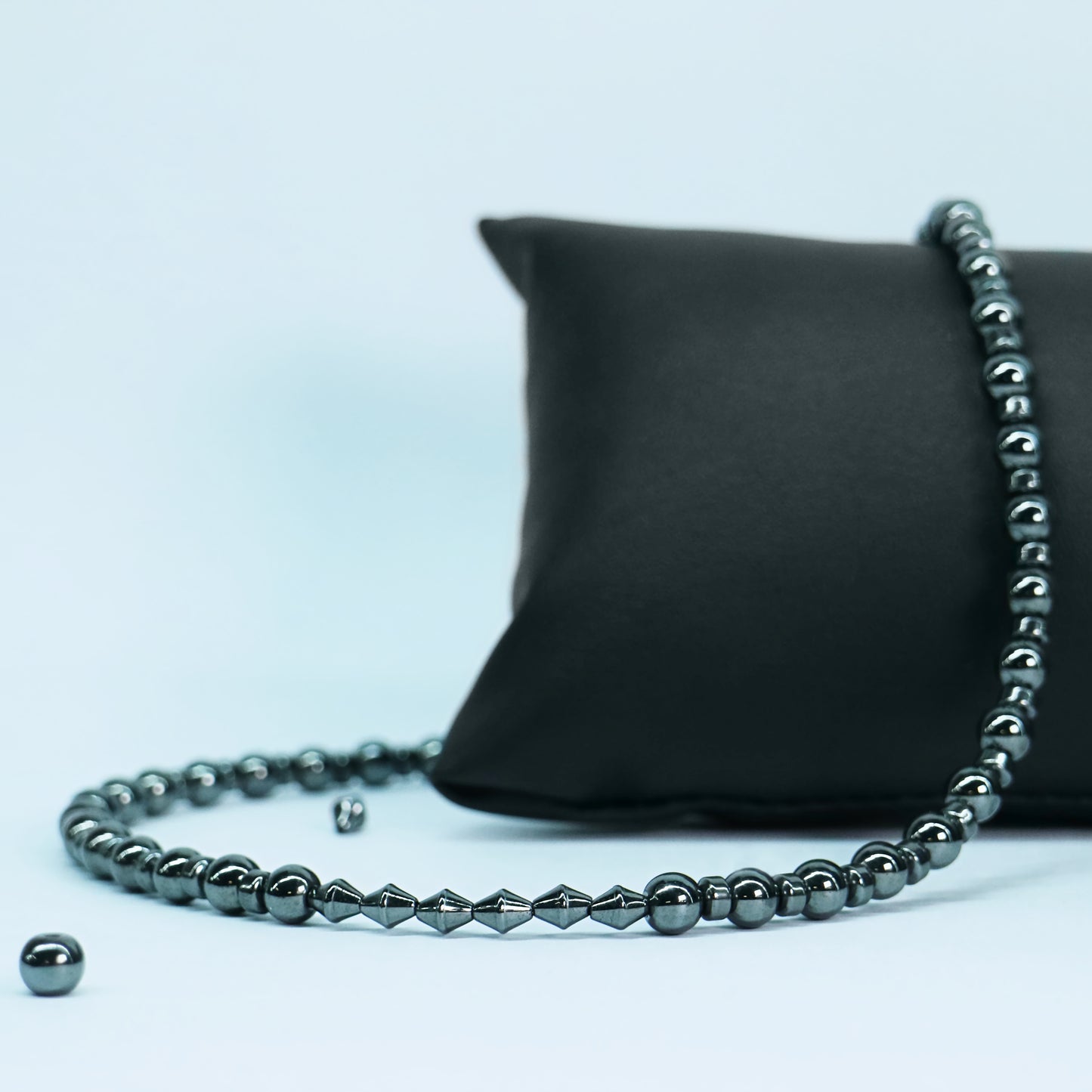 Full view of a white stone and silver hematite bead necklace with a stainless steel boxchain O-ring centerpiece displayed on a black pillow.