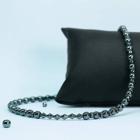 Full view of a white stone and silver hematite bead necklace with a stainless steel boxchain O-ring centerpiece displayed on a black pillow.