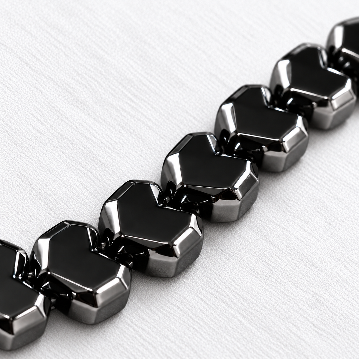 Close-up of HARDLINE's glossy gunmetal hematite pixel heart beads, showing their angular edges on white fabric.