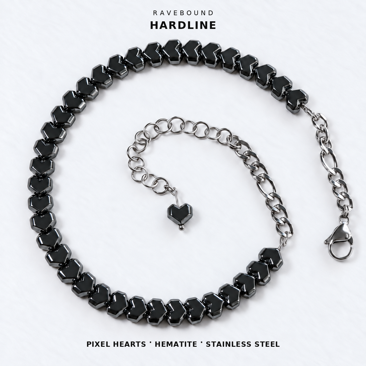 HARDLINE gunmetal pixel heart hematite choker with stainless steel rear chains, lobster clasp and heart-tipped extension on white fabric, with the product name and materials printed above and below.