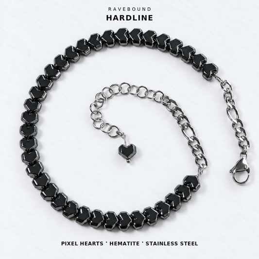 HARDLINE gunmetal pixel heart hematite choker with stainless steel rear chains, lobster clasp and heart-tipped extension on white fabric, with the product name and materials printed above and below.