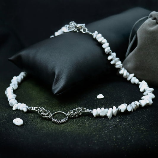 Handmade white stone necklace with stainless steel chainmail O-ring centerpiece displayed on a black cushion