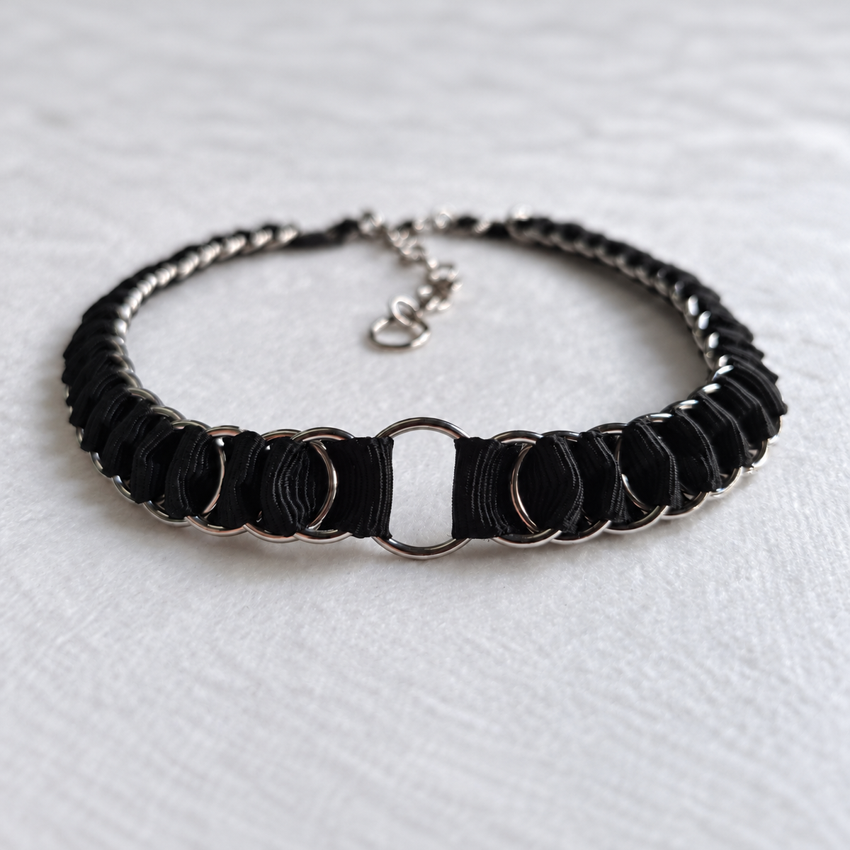 LOOM black fabric ribbon chainmail choker in a low-angle view, with stainless steel rings, a central O-ring and adjustable fastening on white fabric.
