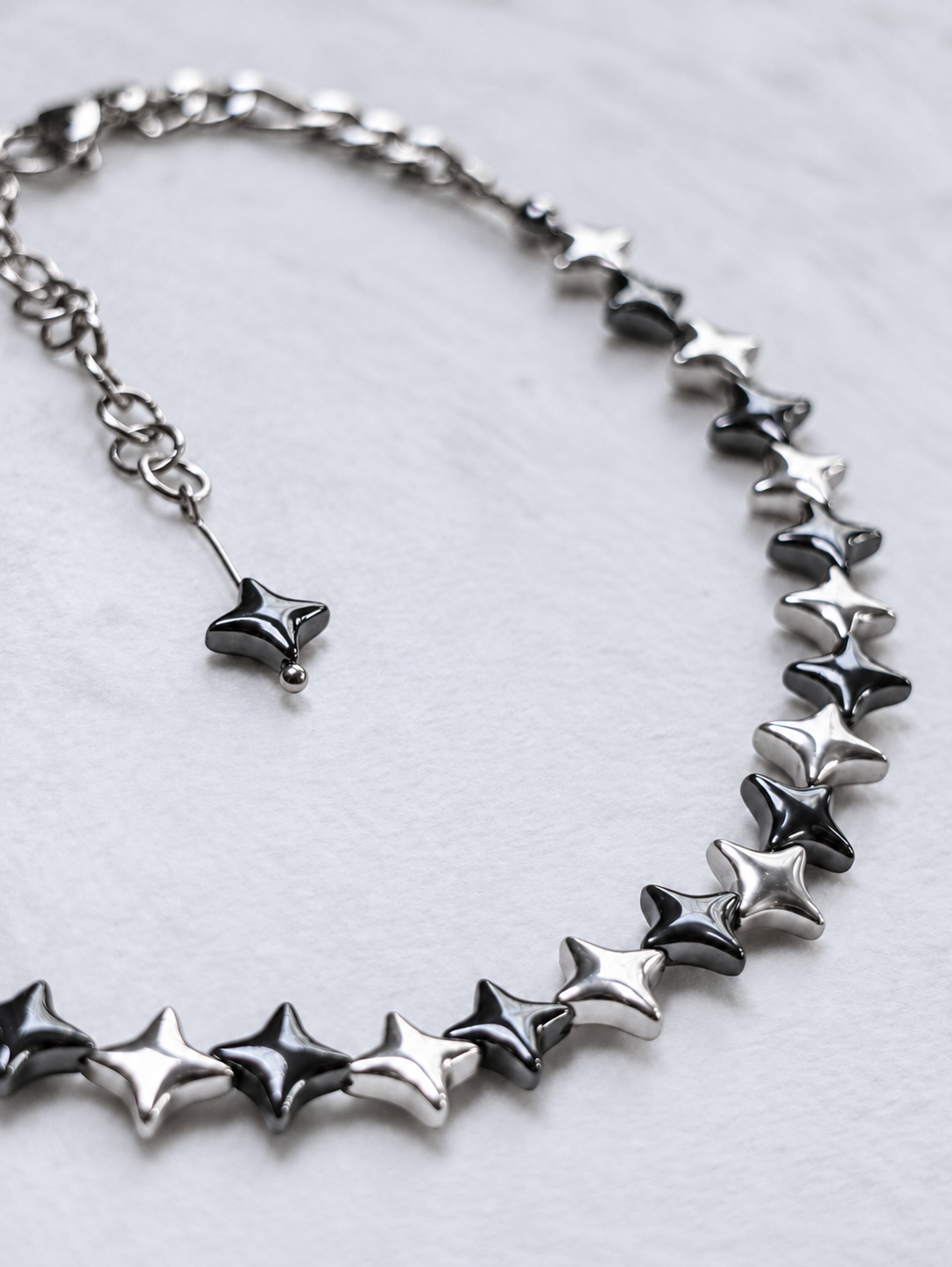 Close-up of NORTHLINE Mixed polished silver and gunmetal hematite stars and stainless steel chains.