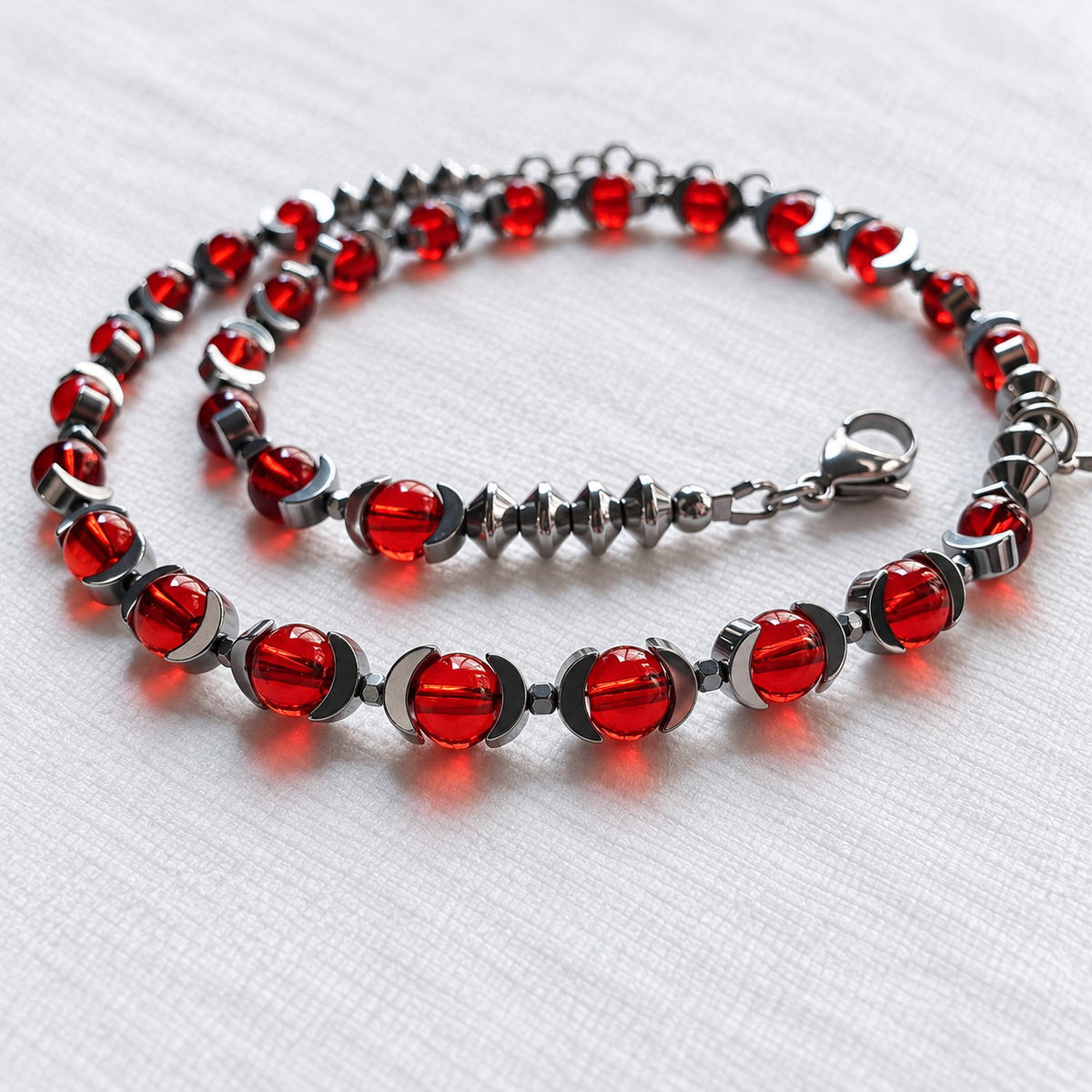Close-up of CELESTIA translucent red glass beads, half-moon hematite and spinning-top hematite beads.
