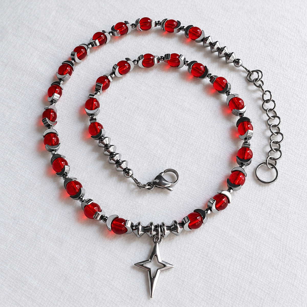 Overhead view of CELESTIA red glass necklace, silver hematite beads, North Star pendant and extension chain.