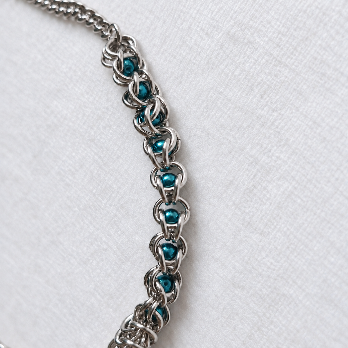 Close-up of ECHO teal glass pearls and interlocking stainless steel rings.