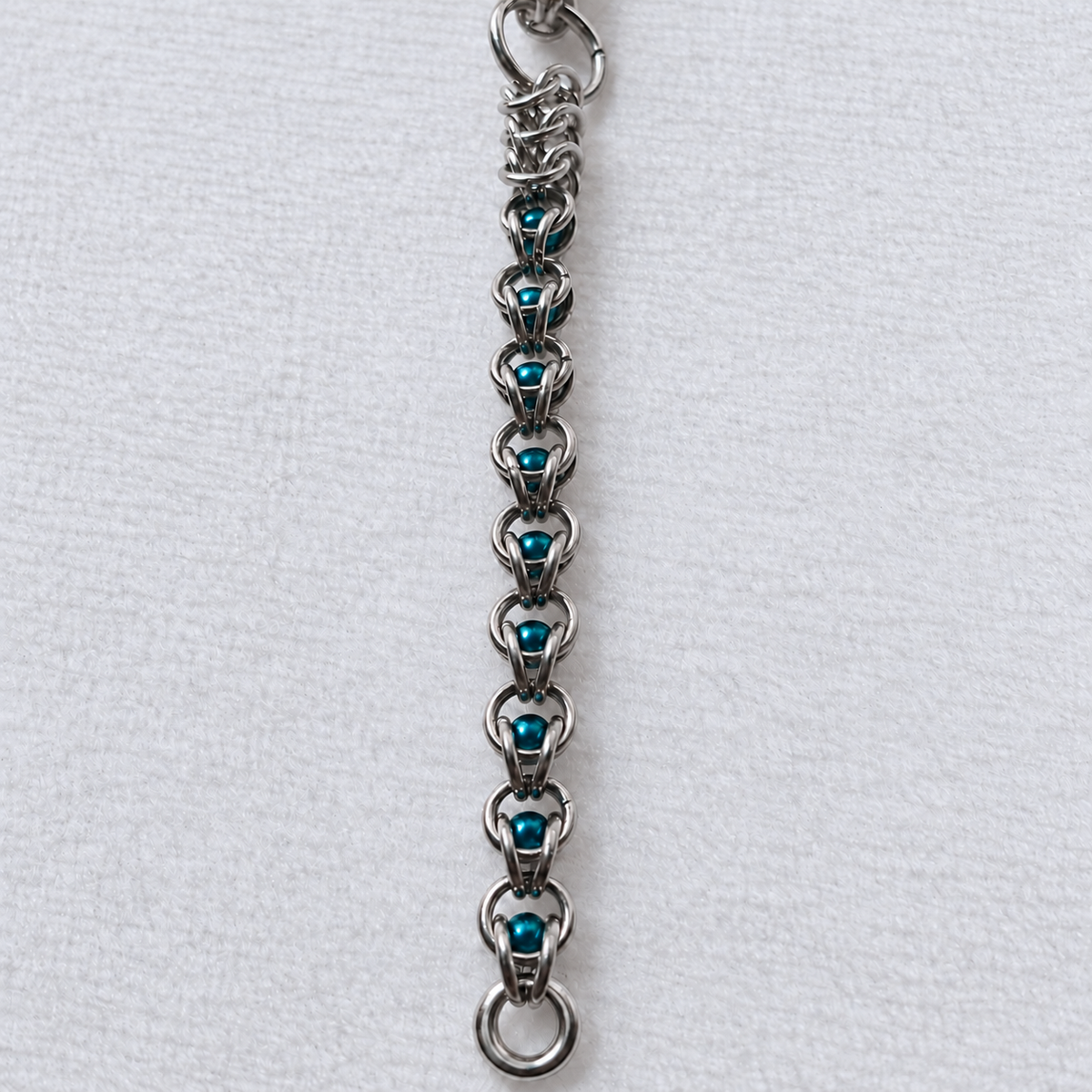 ECHO teal glass pearl beads captured in stainless steel chainmail, vertical detail.