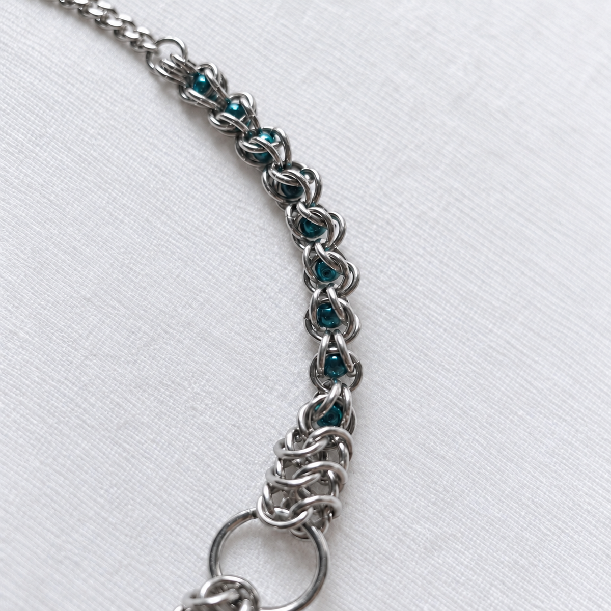 Curved side view of ECHO's teal glass pearl beads and stainless steel chainmail.