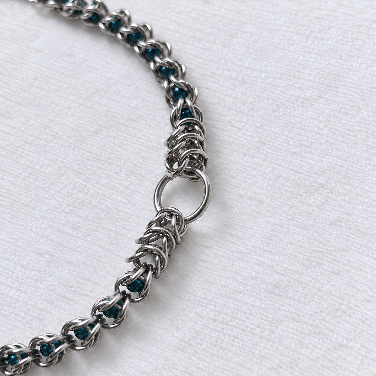 Diagonal close-up of ECHO's front O-ring, stainless steel weave and teal glass pearls.