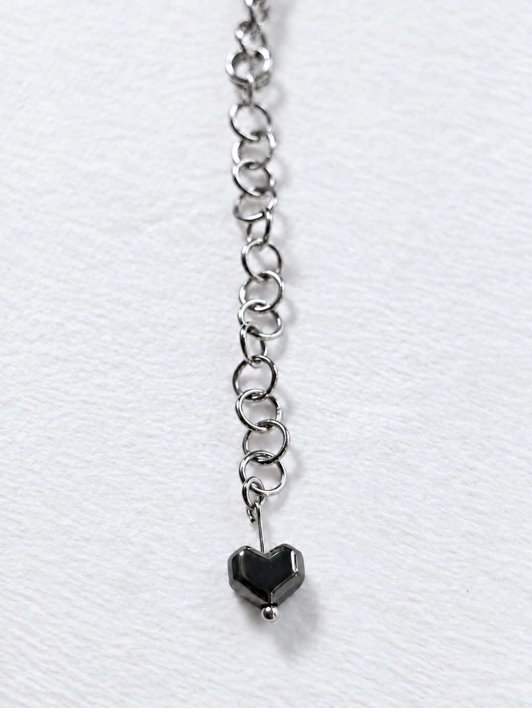Detail of HARDLINE’s stainless steel extension chain ending in a glossy gunmetal hematite heart bead.