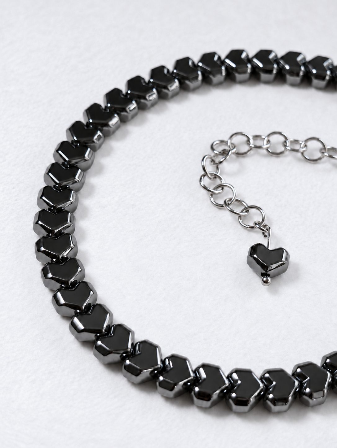Close-up of glossy gunmetal Pixel hematite heart beads and the matching heart at the end of HARDLINE’s stainless steel extension chain.