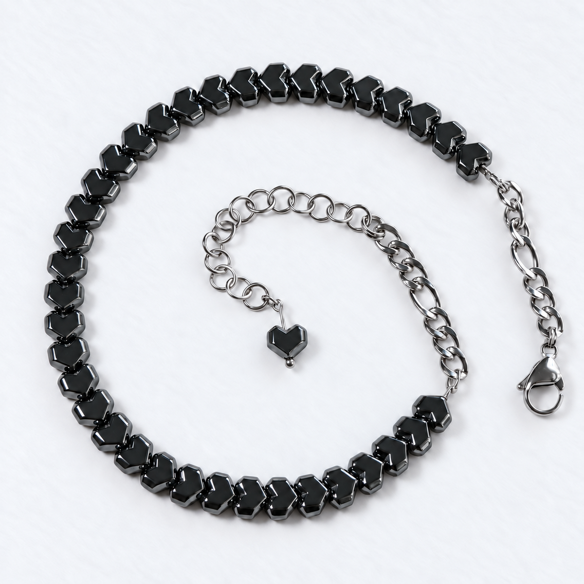 HARDLINE gunmetal Pixel heart hematite choker with stainless steel rear chains, lobster clasp and adjustable extension on white fabric.