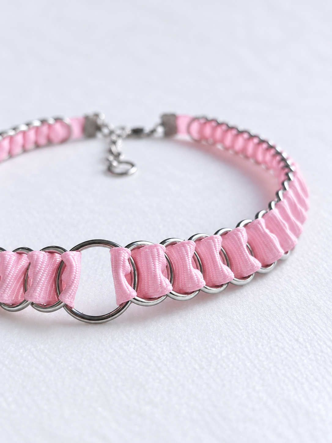 Angled close-up of folded baby pink ribbon and the central stainless steel O-ring on the LOOM choker.