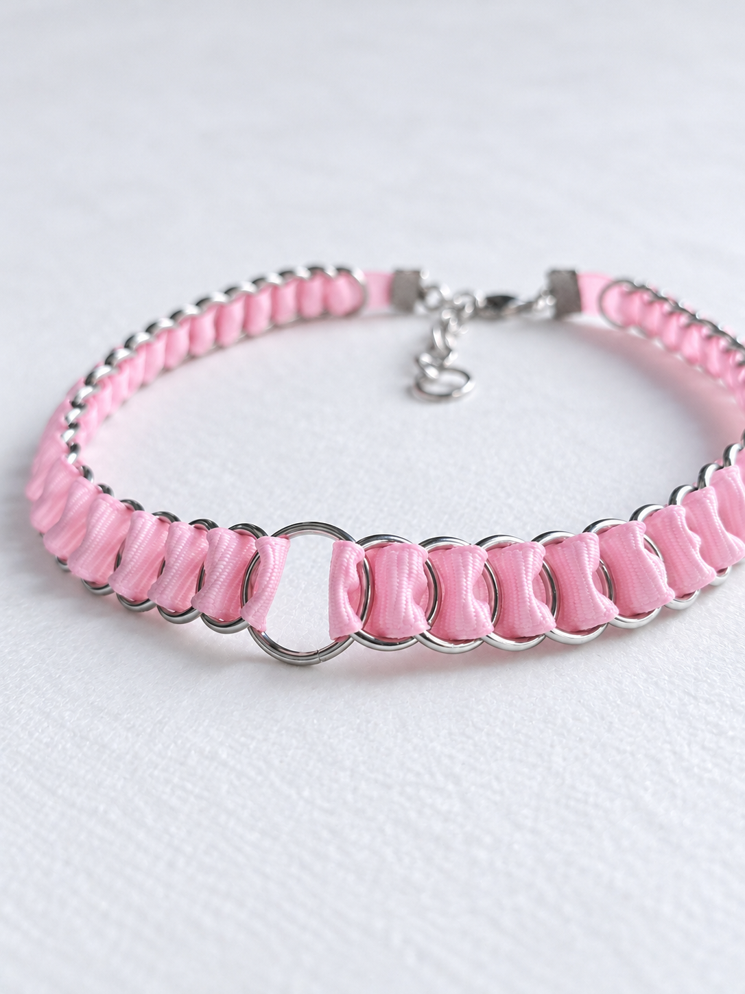 Angled view of the LOOM baby pink ribbon chainmail choker with stainless steel O-ring and extension chain.