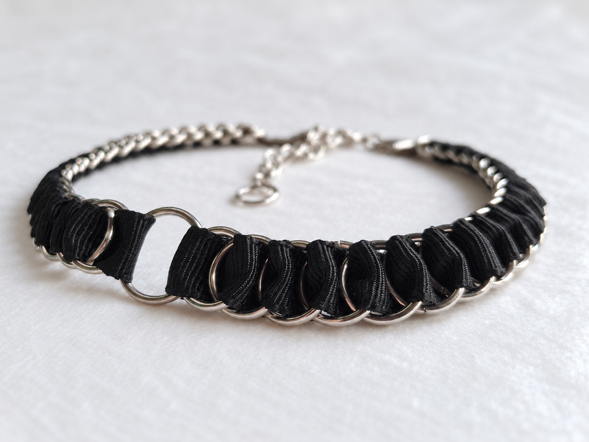 Low-angle detail of the LOOM black choker showing folded fabric ribbon and interlinked stainless steel rings.