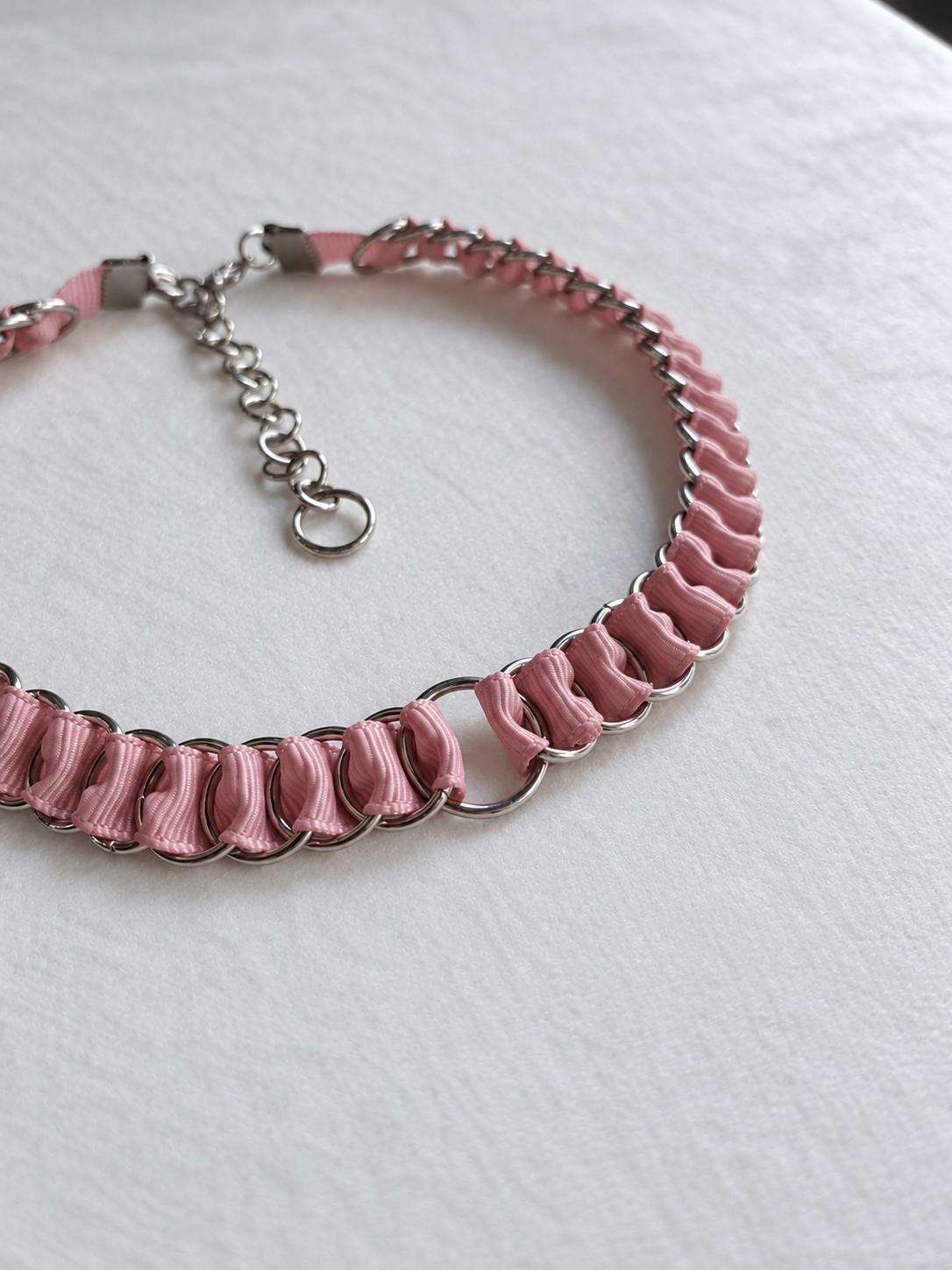 Angled close-up of dusty pink ribbon woven through stainless steel rings and the central O-ring on the LOOM choker.