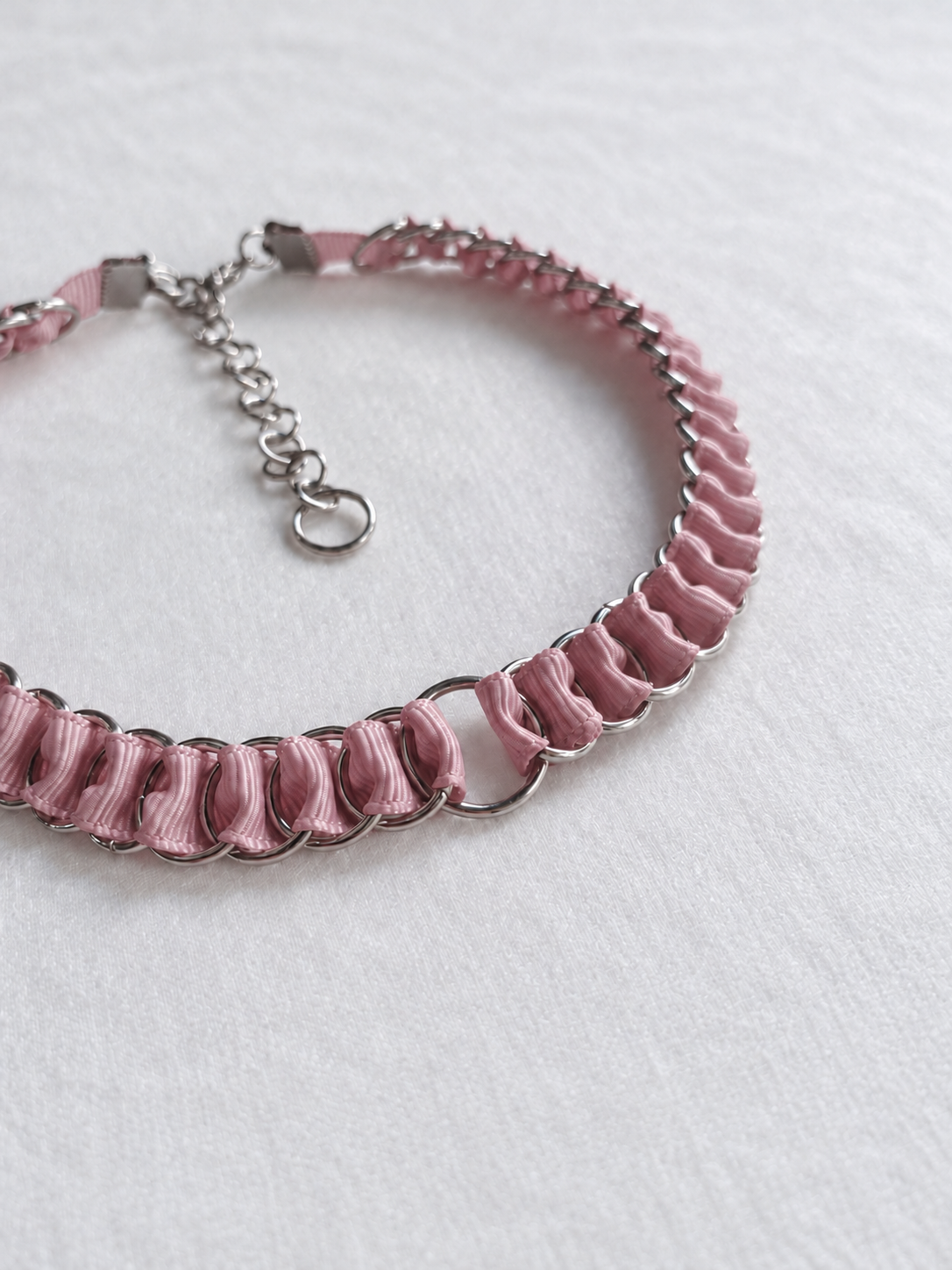 Angled close-up of dusty pink fabric ribbon woven through stainless steel rings on the LOOM choker.
