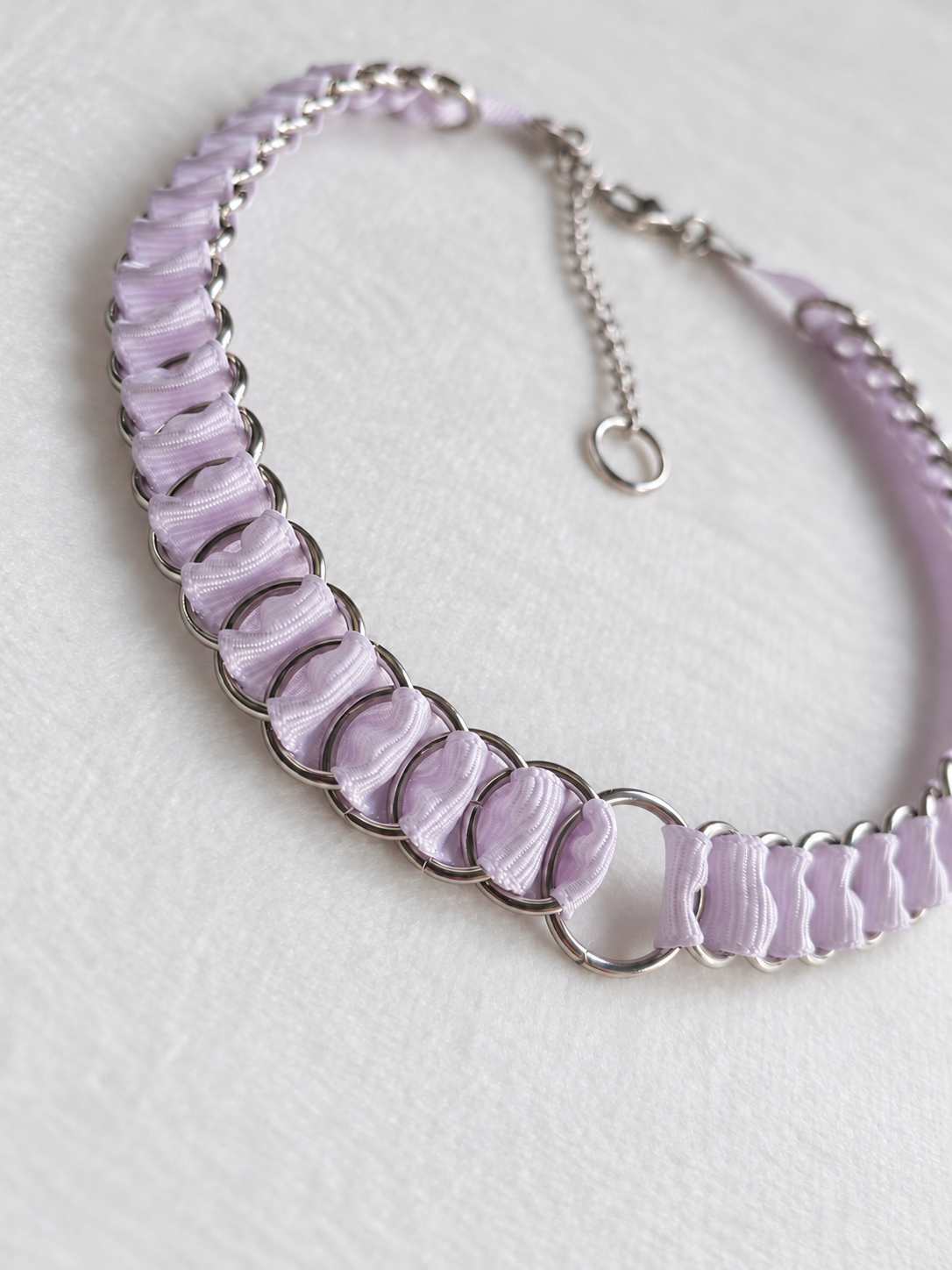 Angled detail of lilac fabric ribbon woven through stainless steel rings and the central O-ring on the LOOM choker.