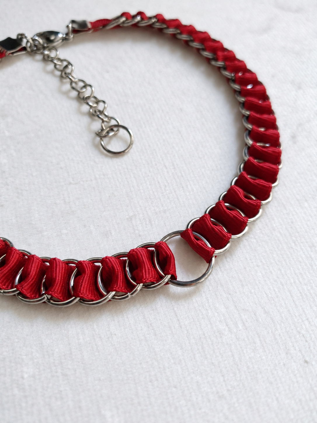 Angled close-up of the LOOM red choker showing the central stainless steel O-ring and folded fabric ribbon.