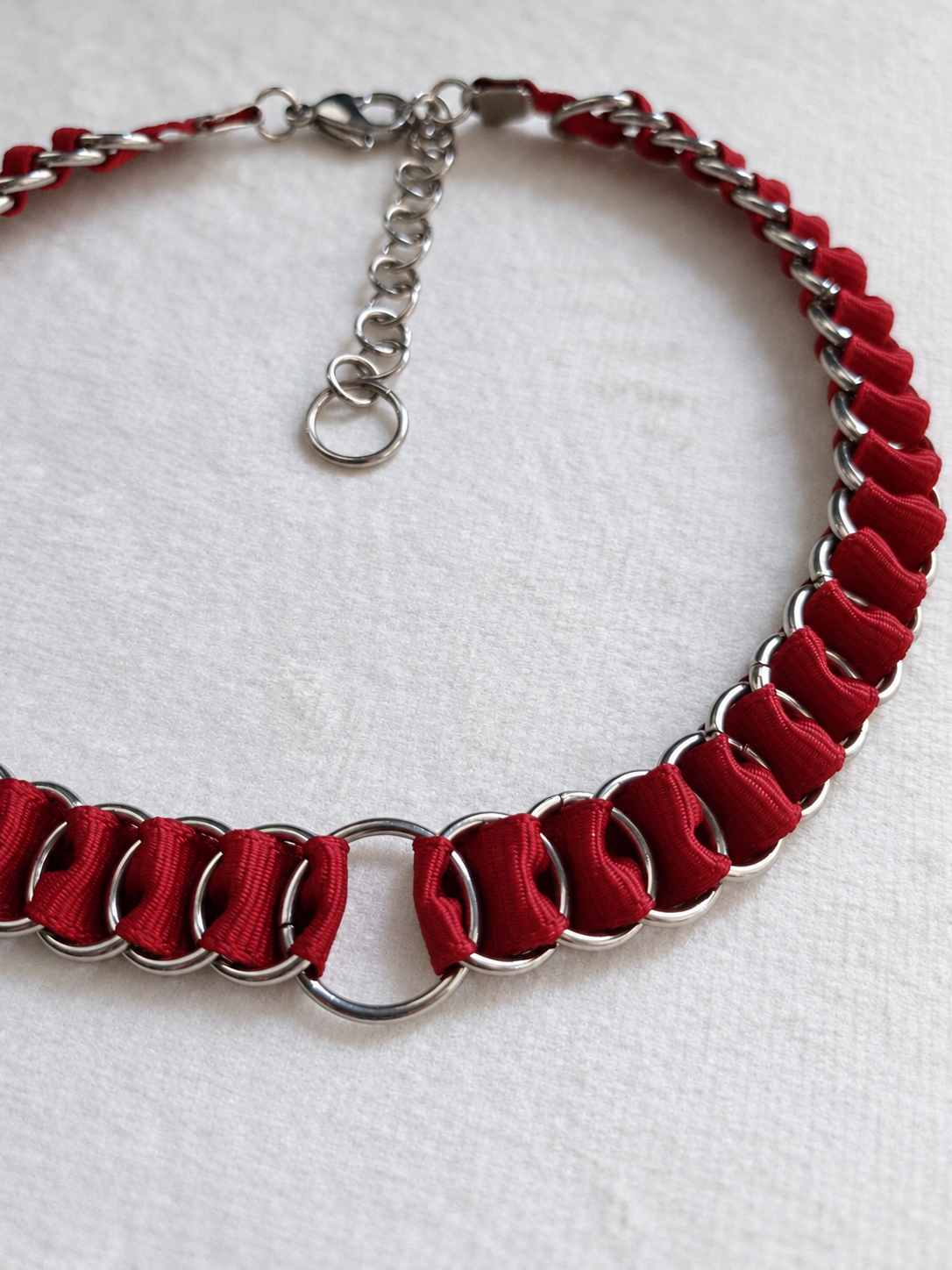 Close-up of the central stainless steel O-ring and red fabric ribbon weave on the LOOM chainmail choker.