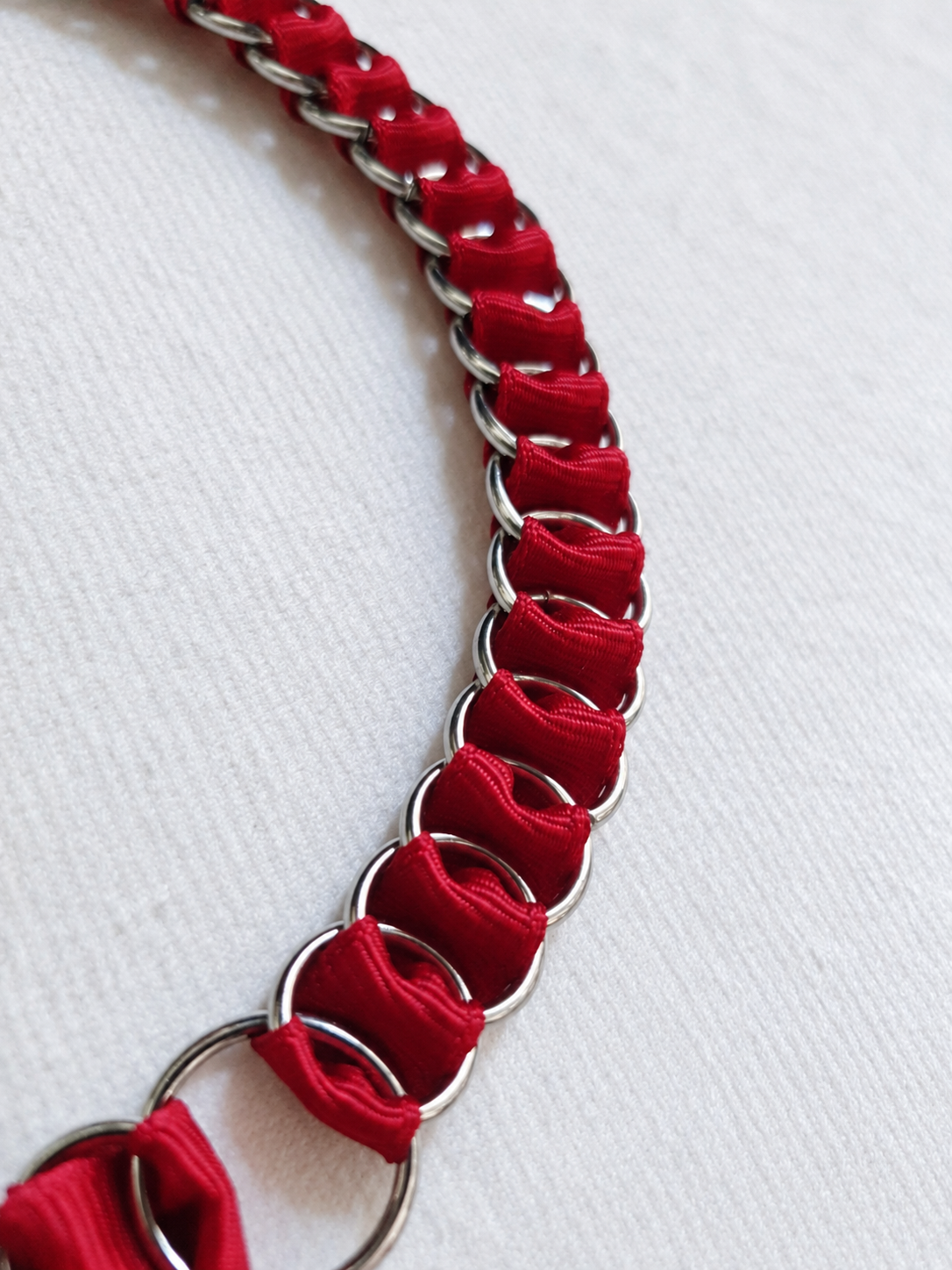Detail of red fabric ribbon woven through interlinked stainless steel rings on the LOOM choker.