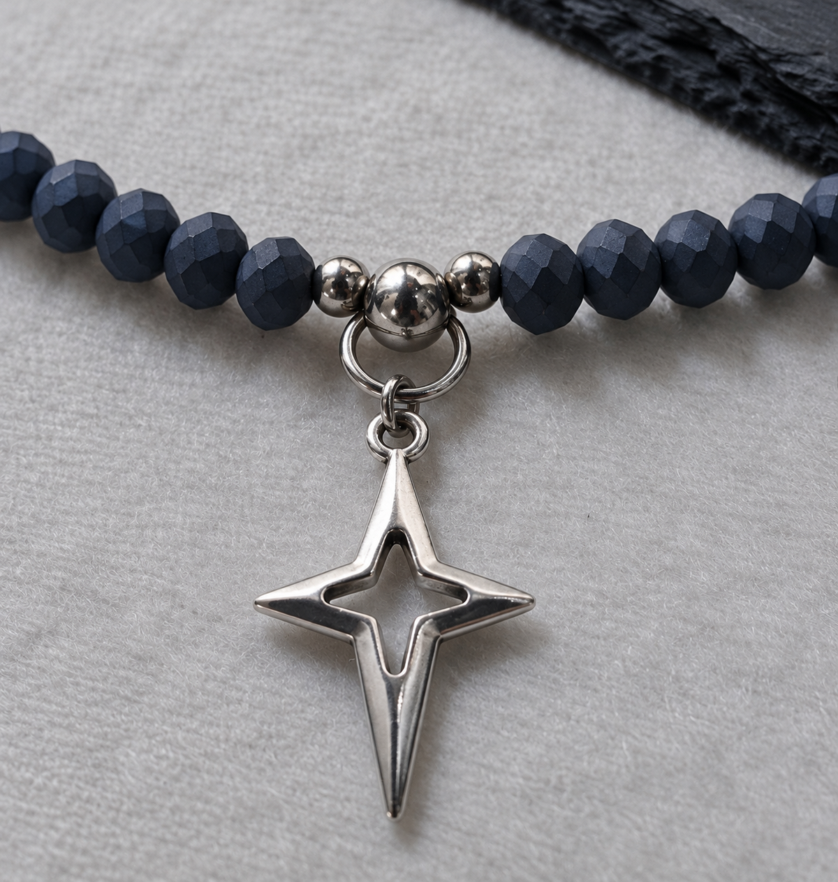 Close-up of NIGHTMARK's silver-plated North Star pendant, ring connector and faceted matte midnight blue crystal beads.